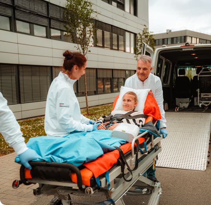 Patiententransport mit Pflegekräften vor Klinikgebäude.